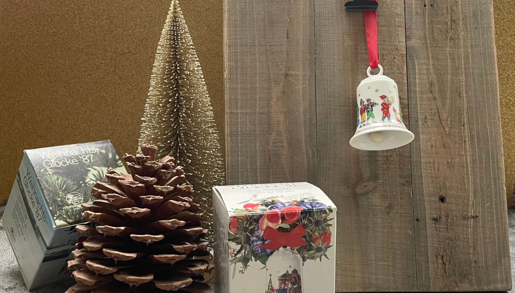 Hutschenreuther Weihnachtsglocke vor einem Hintergrund aus Holz neben einem goldenen Dekotannenbaum