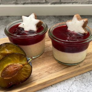 2 kleine Gläser Weihnachtsdessert mit Zwetschgenröster und Zimtstern. im Vordergrund eine geöffnete Zwetschge.