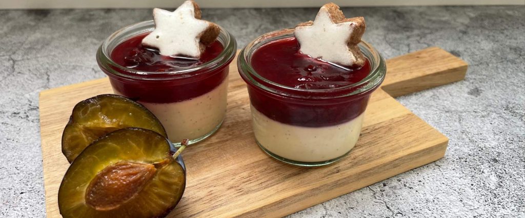 2 kleine Gläser Weihnachtsdessert mit Zwetschgenröster und Zimtstern. im Vordergrund eine geöffnete Zwetschge.